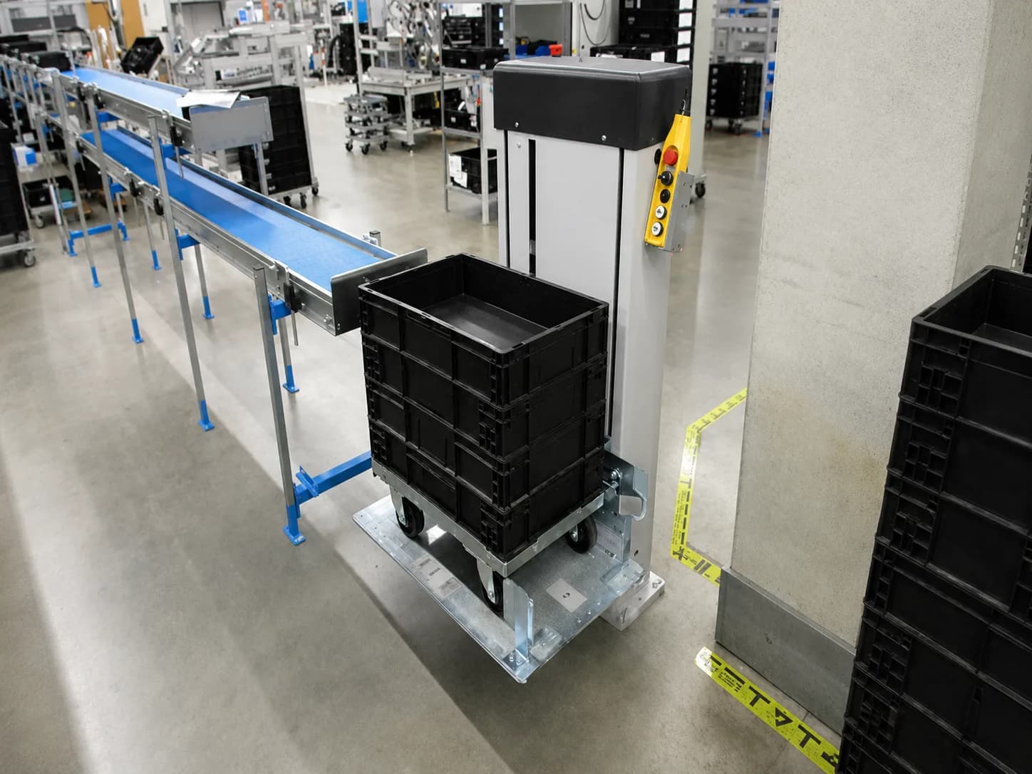 Vertical pallet lift handling stacked tote boxes beside a production conveyor
